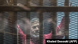 EGYPT -- Egyptian ousted Islamist president Muhammad Morsi, wearing a red uniform, gestures from behind the bars during his trial in Cairo at the police academy, April 23, 2016