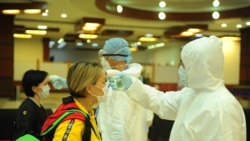 Сотрудники в защитных костюмах замеряют температуру пассажиров в аэропорту Бишкека.