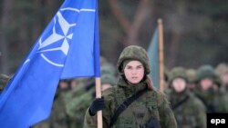 O femeie soldat prezintă drapelul NATO la ceremonia de închidere a exercițiului militar multinațional Iron Sword 16 în apropiere de Vilnius, 2 decembrie 2016