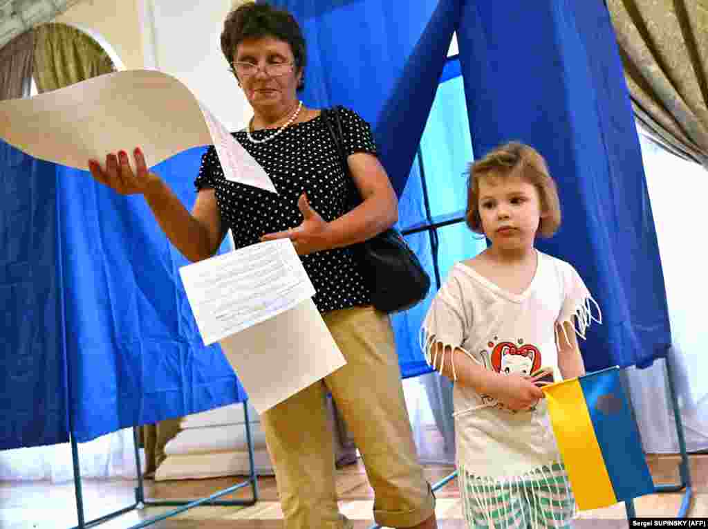 A girl holds the Ukrainian flag as her grandmother examines ballot papers at a polling station in Kyiv. (AFP/Sergei Supinsky)