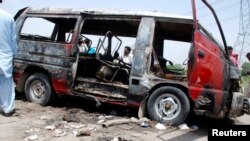 Men stand around a burnt-out school bus after a gas cylinder on it exploded, killing seventeen people, on the outskirts of Gujrat,Pakistan. 