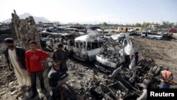 Residents stand at the site of yesterday's suicide car bomb attack on a government security building in Kabul on April 20.