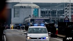 A Belgian police vehicle driving past passengers who are evacuating the Brussels Airport of Zaventem.