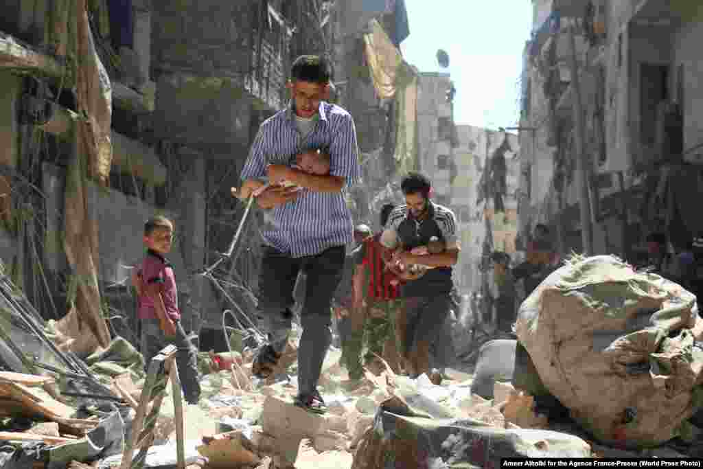 Syrian men carrying babies make their way through the rubble of destroyed buildings following a reported airstrike on the rebel-held al-Salihin neighborhood of Aleppo on September 11, 2016.&nbsp; Spot News -- First Prize, Stories (Ameer Alhalbi for AFP)