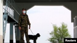 A masked border guard with a canine stands at an empty vehicle checkpoint at the Korgas crossing point, the largest on the 1,500-kilometer Kazakh-Chinese border in May.