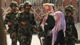 Группа уйгурских женщин-мусульманок на фоне патруля китайской армии. Урумчи, 2016 год
