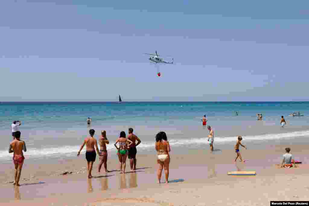 Ljudi na plaži kod Tarife na jugu Španije gledaju kako helikopteri kupe vodu za gašenje požara.Hiljade ljudi evakuisane su iz kuća i hotele, uključujući i turiste na plažama na jugu Španije.