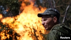 An armed pro-Russian separatist looks on as flames erupt from a gas pipeline after a shelling in Donetsk on August 15.