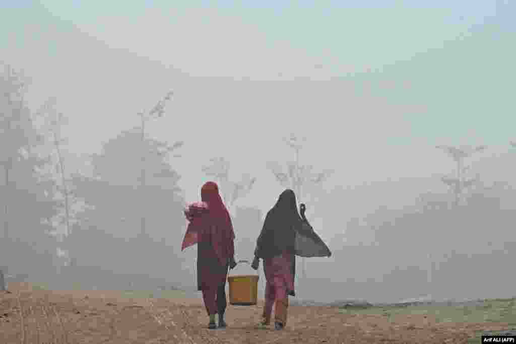 Pakistani women carry a bucket of water along a path engulfed in smog in Lahore.