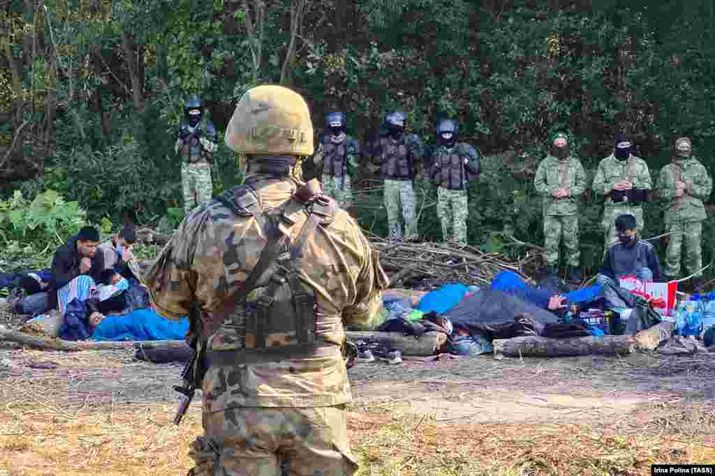 The group of migrants, photographed between an armed Polish serviceman (in foreground) and Belarusian police. The standoff comes amid a surge in mostly Middle Eastern migrants entering the EU illegally from Belarus. European authorities accuse Minsk of deliberately engineering the crisis as a reaction to sanctions imposed by the EU since Belarusian strongman Alyaksandr Lukashenka&#39;s crackdown began following a disputed election one year ago.