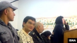 آمنه بهرامی‌نوا (راست، ایستاده) و مجید موحدی (نشسته بین دو سرباز) در جلسه دادگاه