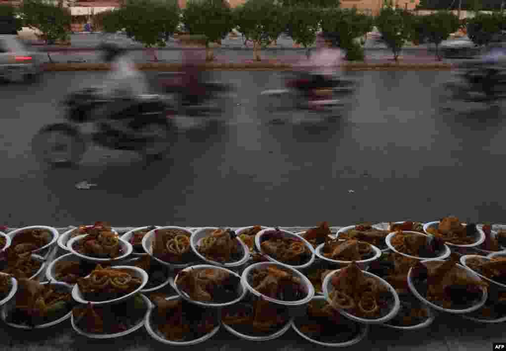 Karaçi, agyz açylýan wagty ýaşaýjylar üçin goýlan naharly tabaklaryň gapdalyndan geçip barýan motorlylar. Pakistan. (AFP/Asif Hassan)