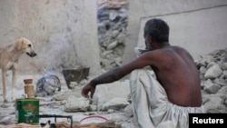 An Awaran man drinks tea as he sits in what remains of his house.