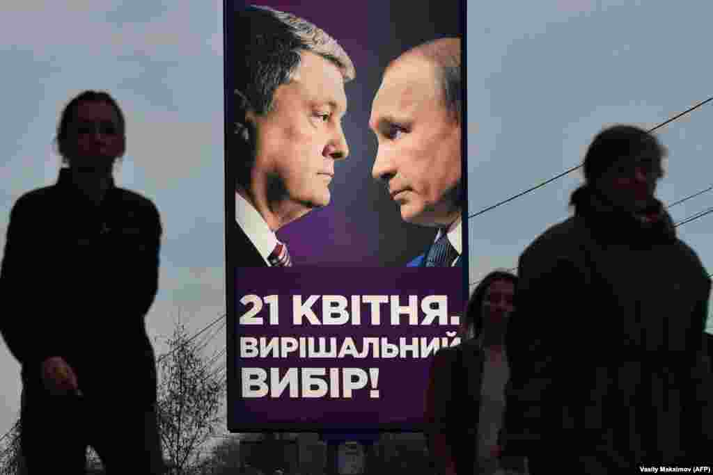 People in Kyiv walk past an election-campaign poster showing the current Ukrainian President Petro Poroshenko facing Russian President Vladimir Putin. (AFP/Vasily Maximov)