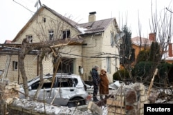 ადგილობრივები დგანან საცხოვრებელ კორპუსთან, რომელიც რუსეთის მიერ უკრაინაზე თავდასხმისას, დრონებითა და რაკეტებით მიტანილი იერიშის შედეგად დაზიანდა. კიევი, უკრაინა, 2026 წლის 22 თებერვალი. REUTERS/ვალენტინ ოგირენკო.