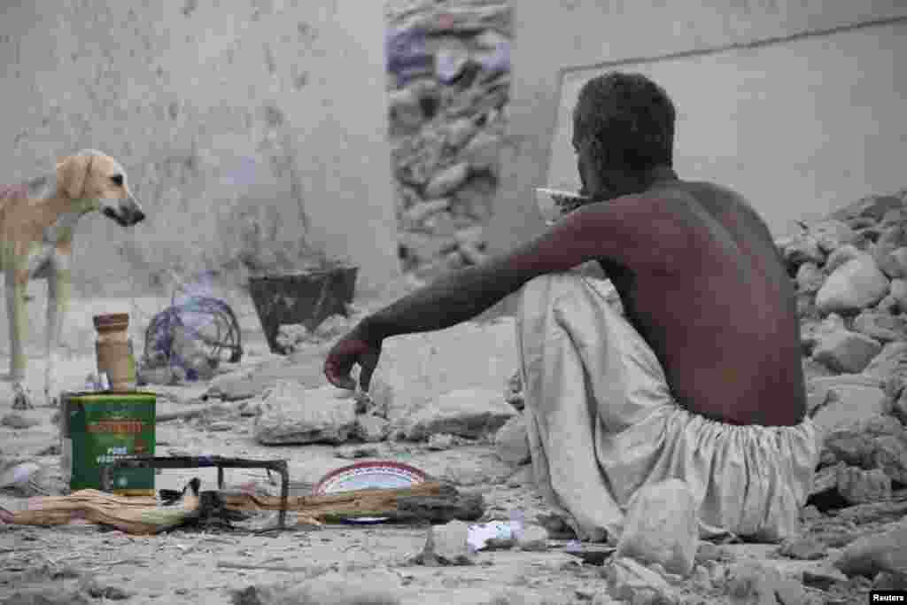 An earthquake survivor sits and drinks tea on the rubble of a mud house in Awaran.