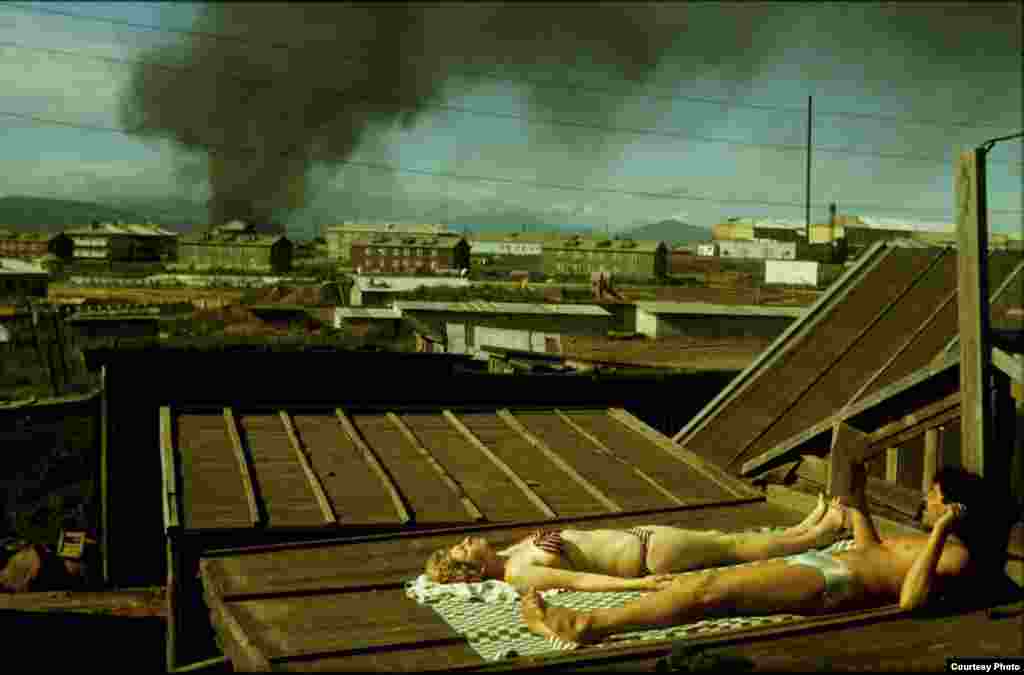 Семейная пара загорает на крыше барака-общежития на фоне дыма горящей свалки, Южнокурильск, 1990. 