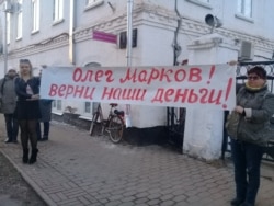 Defrauded investors hold up a sign in Veliky Ustyug, saying Oleg Markov, return our money!