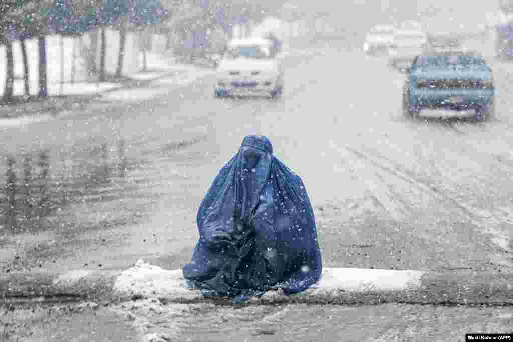 A burqa-clad Afghan woman looks for alms on a street during the first heavy snowfall this winter in Kabul.&nbsp;