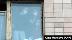 Люди в лицевых масках видны в окне здания, помещенного в карантин, в общежитии Северо-Западного государственного медицинского университета им. И.И. Мечникова