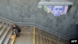 A beggar asks for alms near a torn poster depicting a Ukrainian 200-hryvnya banknote in Kyiv. Economists disagree on the best way to help Ukraine tackle its escalating economic crisis. 