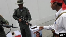 A political activist approaches mock ballot boxes as colleagues dressed as Myanmar soldiers raise their rifles during a mock vote as part of a protest outside the Myanmar Embassy in Bangkok today.