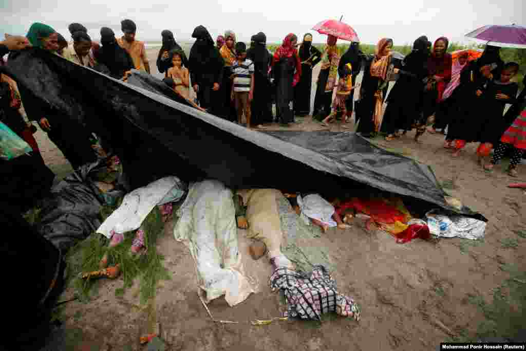 Люди покрывают тела женщин и детей рохинджа, которые умерли после того, как их лодка опрокинулась при пересечении Бенгальского залива, недалеко от Текнафа, Бангладеш.