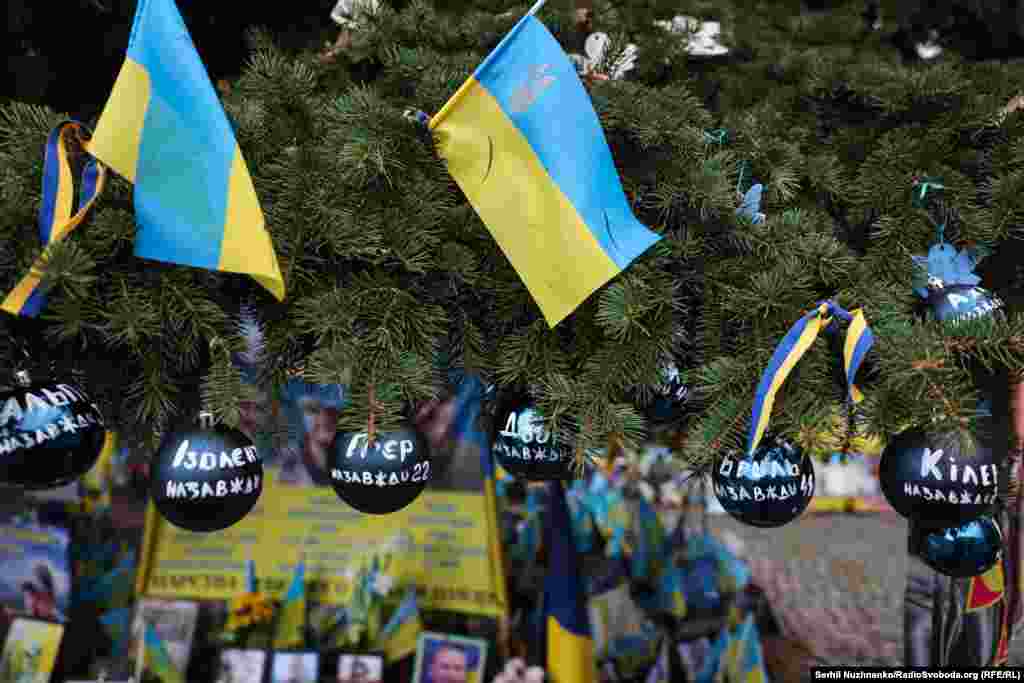 Ялинкові новорічні кульки з позивними загиблих військових на ялині поруч із меморіалом з прапорців на майдані Незалежності