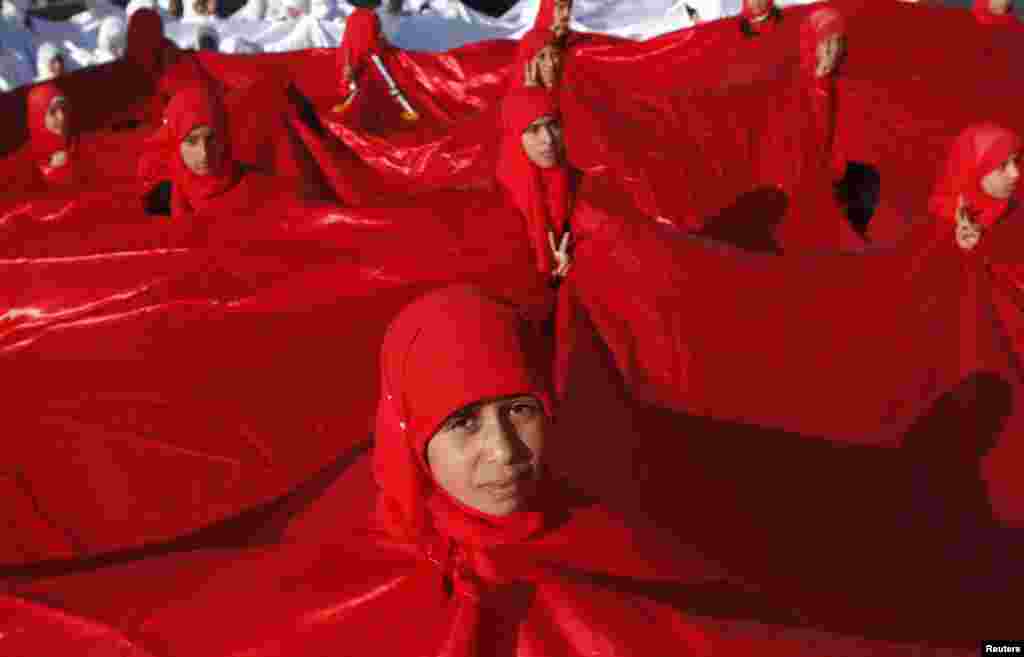 Girls appear through holes in a big national flag as they prepare to take part in a parade commemorating the second anniversary of the uprising against Yemen&#39;s former president, Ali Abdullah Saleh, in Sanaa. (Reuters/Khaled Abdullah)