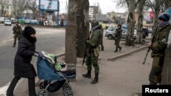 Жінка з дитиною проходить біля бойовиків угруповання «ДНР». Донецьк, березнь 2015 року