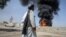 A Taliban fighter walks as smoke rises after Pakistani air strikes hit oil depots for commercial airlines, near the Kandahar airport in March. 