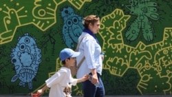 An Iranian woman and a child walk past a mural on a street in Tehran on September 2.
