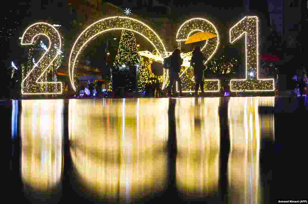 Women walk under an umbrella in front of a 2021 sign displayed in downtown Pristina on December 30. (AFP/Armend Nimani)