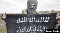 Islamist militant "Abdullah Tajik" posted this photo on social media in February. The black banner he is holding says "The Taliban In The Land Of Sham" ["the Levant"]. 