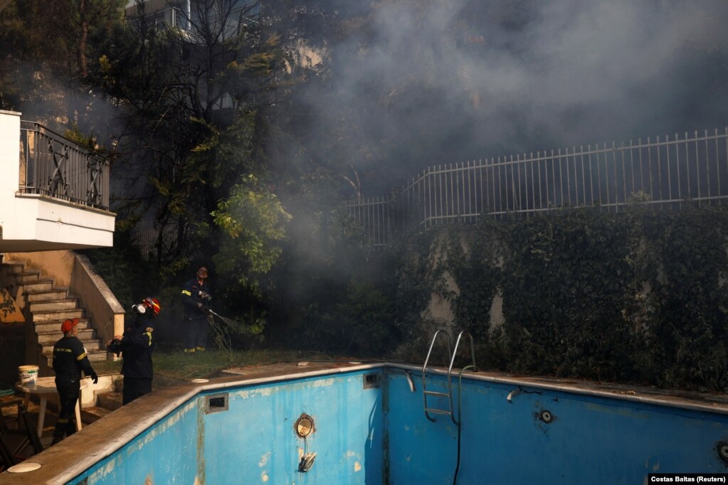 Zjarrfikësit duke hedhur ujë afër një pishine, teksa një zjarr i egër shkrumbonte veriun e Athinës, në Greqi. (7 gusht)