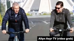 Imagine din 2019, difuzată de televiziunea de stat turkmenă cu Igor Makarov (stânga) și Gurbangulî Berdimuhamedov mergând cu bicicleta prin Așhabad