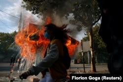 Një person duke ecur pranë një kioske të përfshirë nga flakët gjatë përleshjeve mes policëve dhe demonstruesve, në mes të protestës antiqeveritare në Tiranë, më 15 tetor 2026.