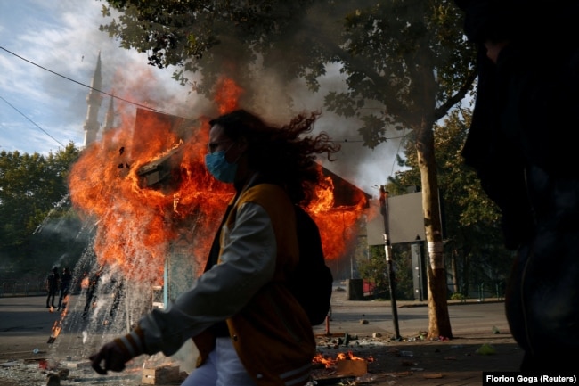 Një person duke ecur pranë një kioske të përfshirë nga flakët gjatë përleshjeve mes policëve dhe demonstruesve, në mes të protestës antiqeveritare në Tiranë, më 15 tetor 2026.