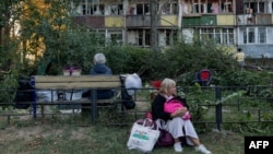 O femeie așezată lângă un bloc avariat în urma unui atac rusesc asupra Kievului, pe 20 august 2026.