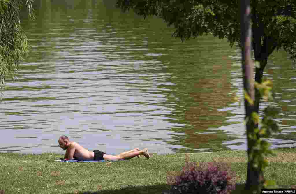 Un bărbat face plajă lângă lacul din Parcul Alexandru Ioan Cuza din București, în pofida avertizărilor medicilor ca populația să evite expunerea voluntară la soare.