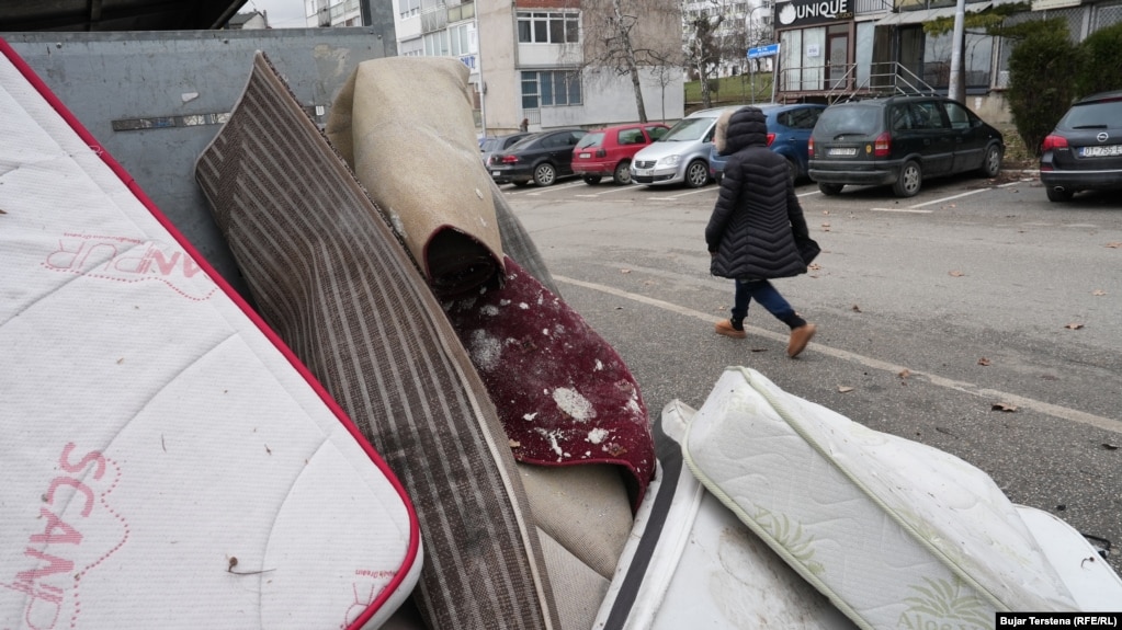 Një qytetare kalon pranë disa dyshekëve dhe gjësendeve të tjera të hedhura pranë një kontejneri në Prishtinë më 26 janar 2026.
