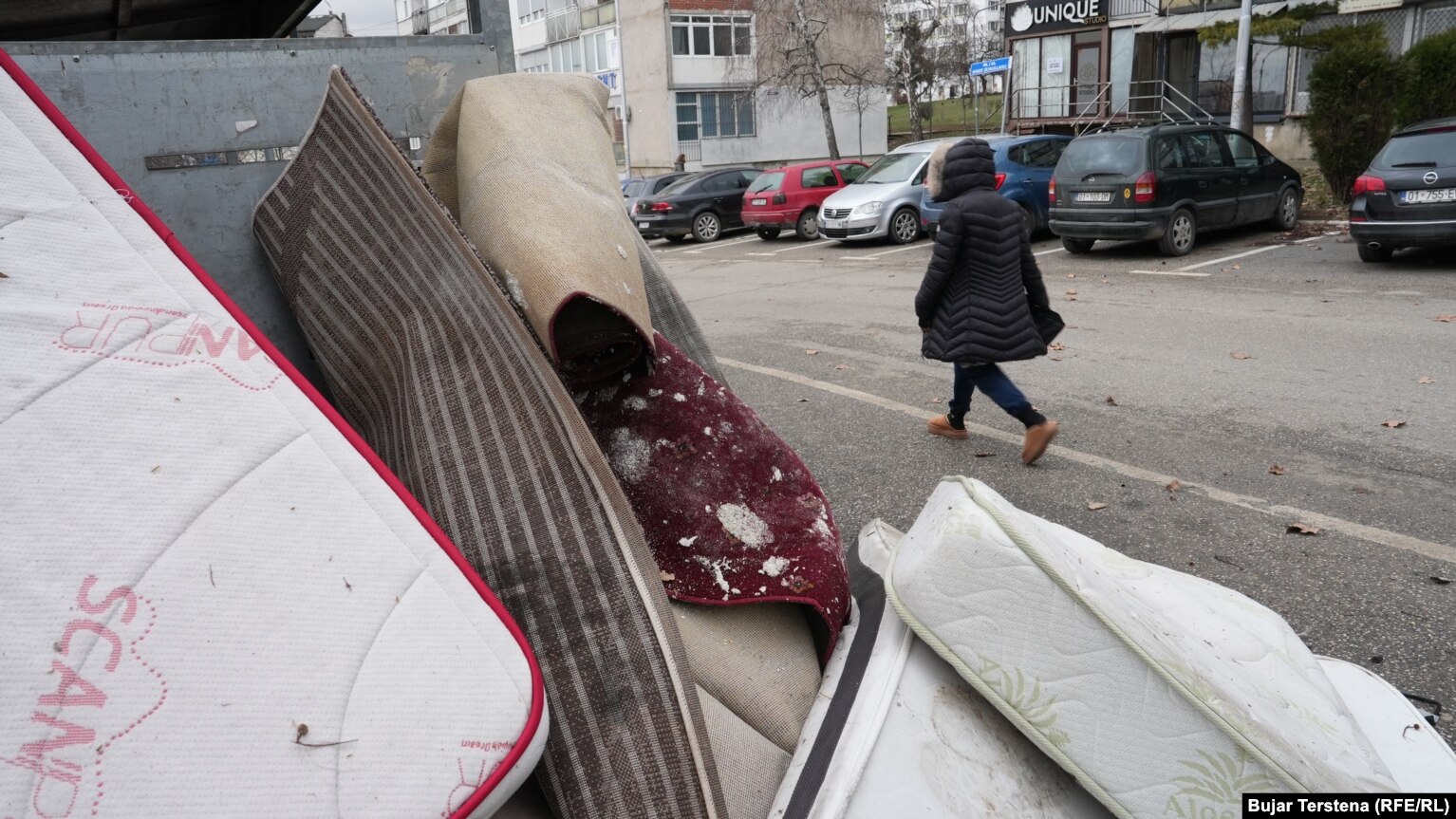 Një qytetare kalon pranë disa dyshekëve dhe gjësendeve të tjera të hedhura pranë një kontejneri në Prishtinë më 26 janar 2026.