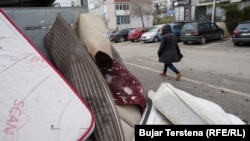 Një qytetare kalon pranë disa dyshekëve dhe gjësendeve të tjera të hedhura pranë një kontejneri në Prishtinë më 26 janar 2026.
