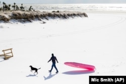 Čovek s psom šeta plažom pod snegom u Južnoj Karolini, 22. januar 2025.