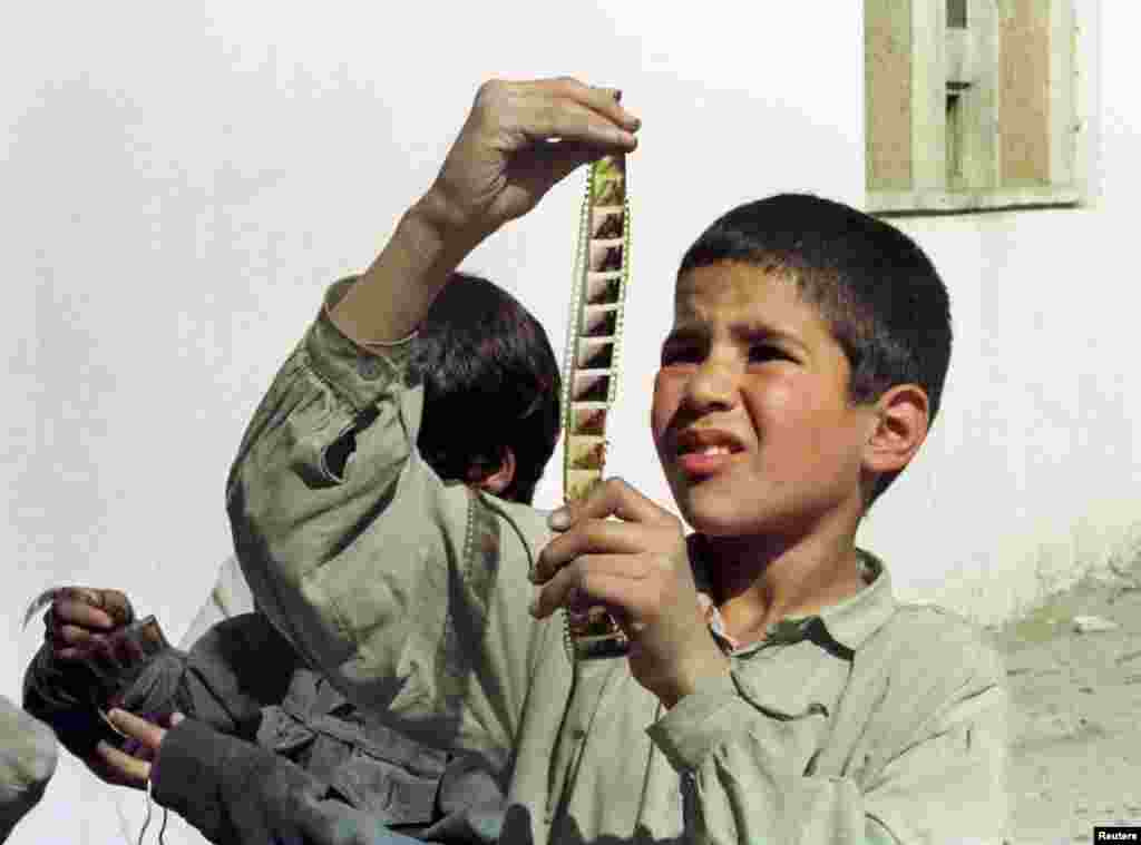 A boy peers at frames from a movie reel he snatched from a bonfire after the Taliban publicly burned movie-screening materials.