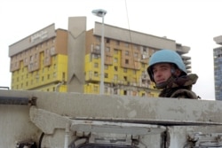 A soldier with the NATO-led multinational Implementation Force (IFOR) stands watch with the badly hit Holiday Inn hotel in the background in December 1995.