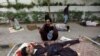 A man uses a hand-held fan to cool down his son while waiting in line for a medical checkup outside a health-center in Karachi.