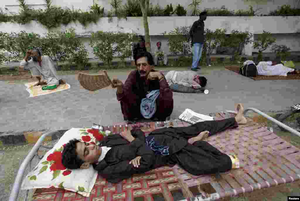 A man uses a hand-held fan to cool down his son while waiting in line for a medical checkup outside a health-center in Karachi.