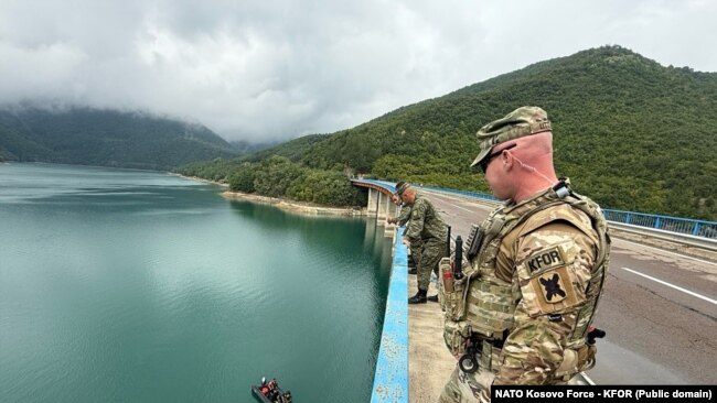 Një ushtar i KFOR-it dhe pjesëtarë të FSK-së qëndrojnë mbi njërën nga urat në Liqenin e Ujmanit, ku më 29 korrik 2025 po zhvillohen kërkime.