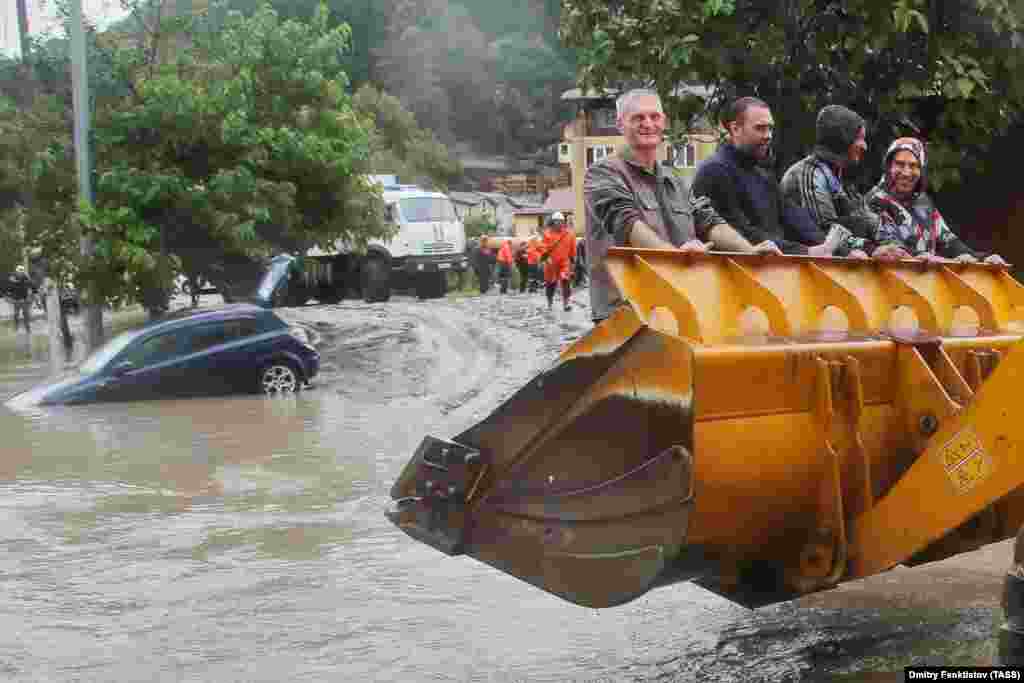 Мужчины залезли в ковш экскаватора в пострадавшем от наводнения районе российского Сочи. Сильные дожди вызвали резкий скачок уровня воды в местных реках